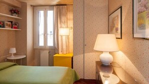 A bedroom with a bed, a bedside table with a lamp, a window with curtains, a radiator, and a wardrobe. - BEAUTIFUL ROMAN APARTMENT NEXT TO TREVI FOUNTAIN (Roma)