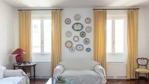 A room with a bed, a chair, a table with a lamp, and a wall decorated with plates. - BEAUTIFUL ROMAN APARTMENT NEXT TO TREVI FOUNTAIN (Roma)