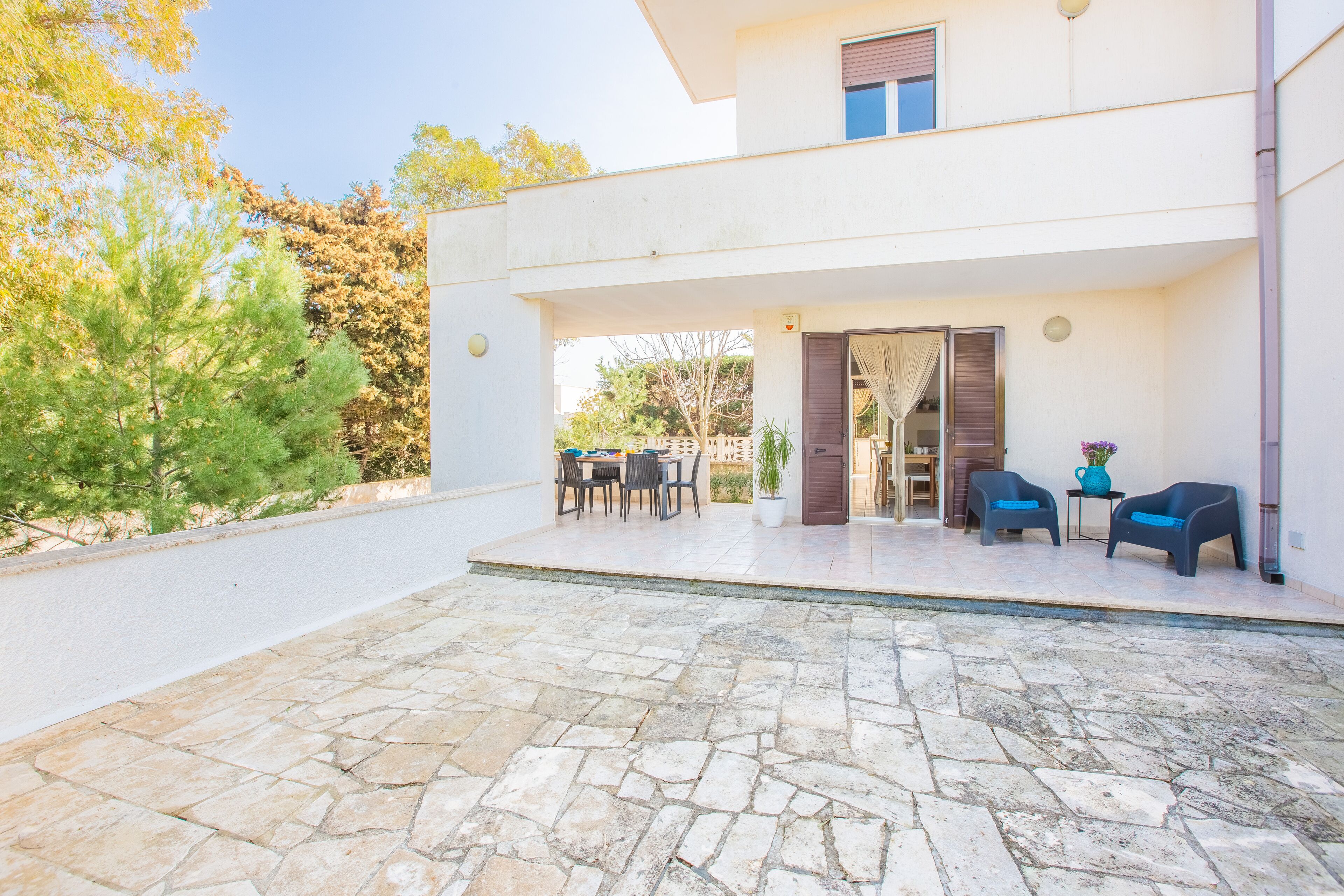 Une maison moderne dotée d’un patio en pierre, d’un espace salon extérieur et offrant une vue sur les arbres.
