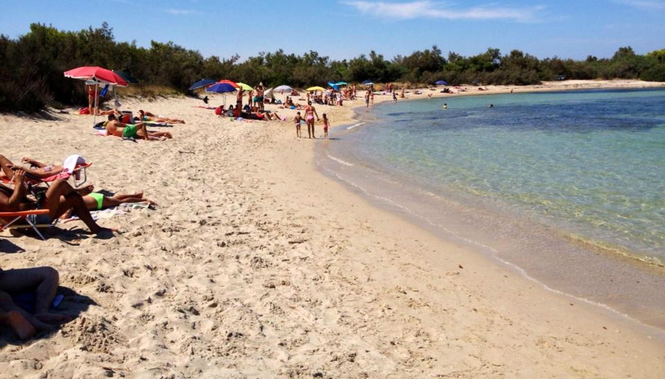 Escena de platja amb persones prenent el sol i banyant-se.