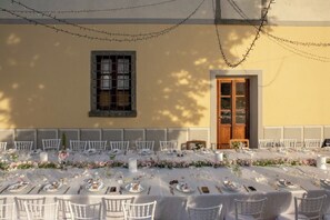 Ein Essbereich im Freien mit gedeckten Tischen, umgeben von weißen Stühlen und geschmückt mit Blumenarrangements.