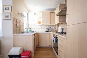Une cuisine de taille réduite, avec des meubles de rangement en bois, un évier, une cuisinière et une poubelle.