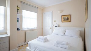 Hotelkamer met een bed, een radiator, een raam met zonwering, een nachtkastje en een schilderij aan de muur.