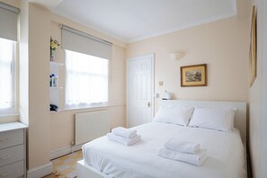 A hotel room with a bed, a radiator, a window with a blind, a bedside table, and a picture on the wall.