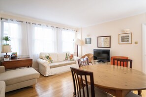 Un salon comprenant un canapé, une table à manger, un téléviseur et deux chaises.
