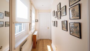 Een gang met aan de wanden ingelijste foto's, een radiator en een deur aan het einde.