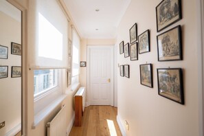 A hallway with framed pictures on the walls, a radiator, and a door at the end.