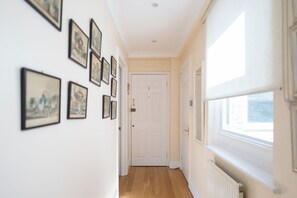Un couloir orné d’une série de tableaux encadrés le long du mur, une porte blanche au fond et une fenêtre sur le côté droit.