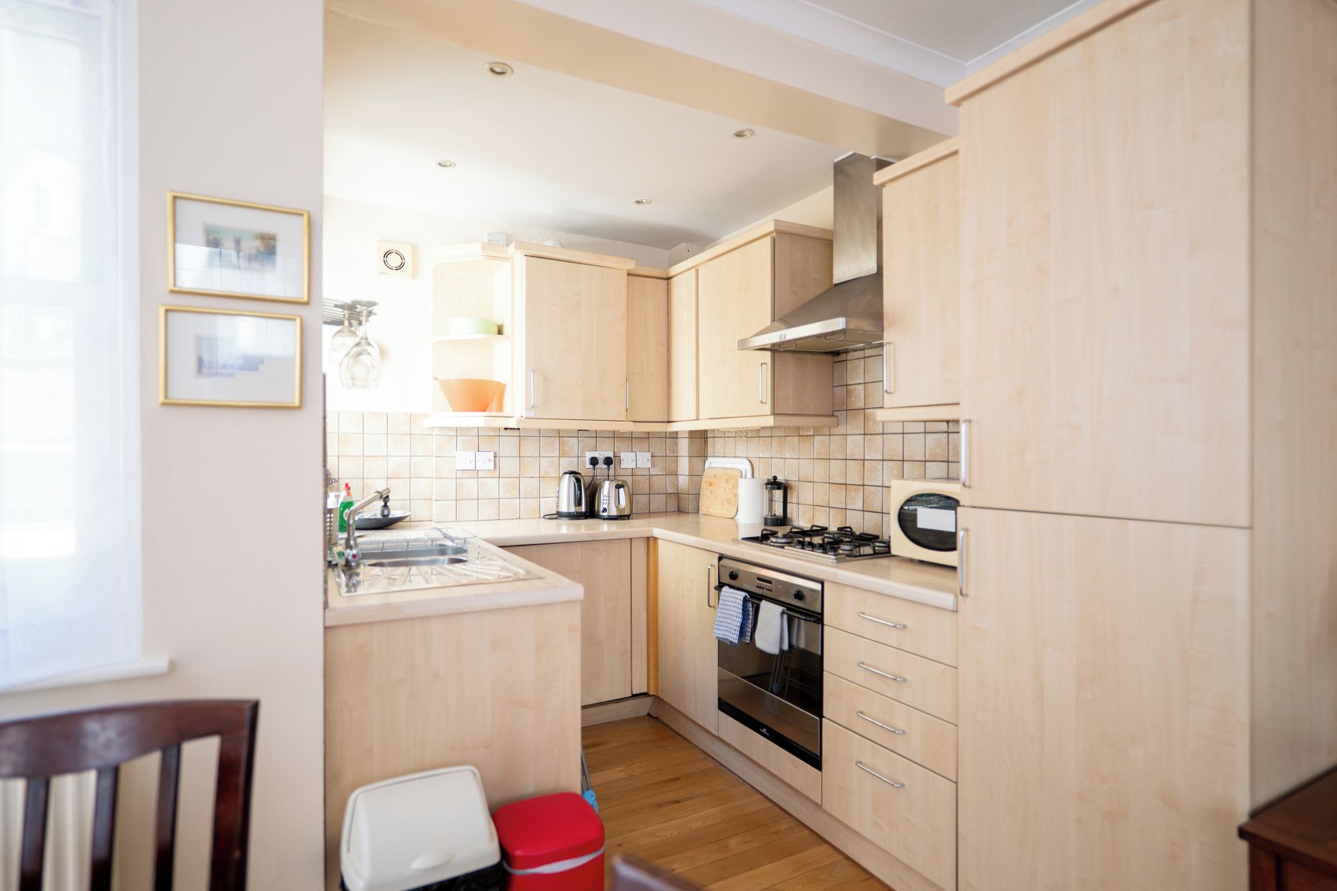 A compact kitchen with light wood cabinetry, a gas stove, a built-in oven, and a sink.