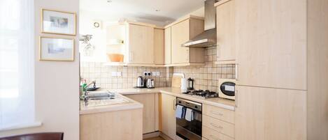 A compact kitchen with light wood cabinetry, a gas stove, a built-in oven, and a sink.