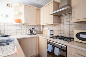 A kitchen with wooden cabinets, a gas stove, a microwave, and a kettle.