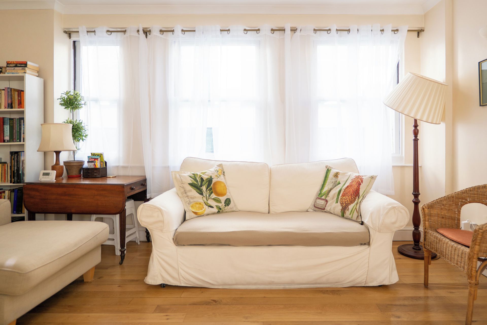 A living room with a sofa, a lamp, a bookshelf, and a window with curtains.