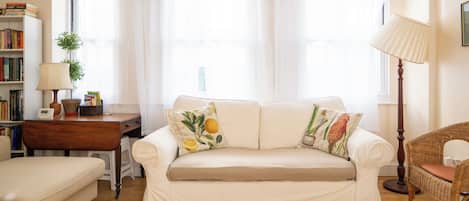 A living room with a sofa, a lamp, a bookshelf, and a window with curtains.