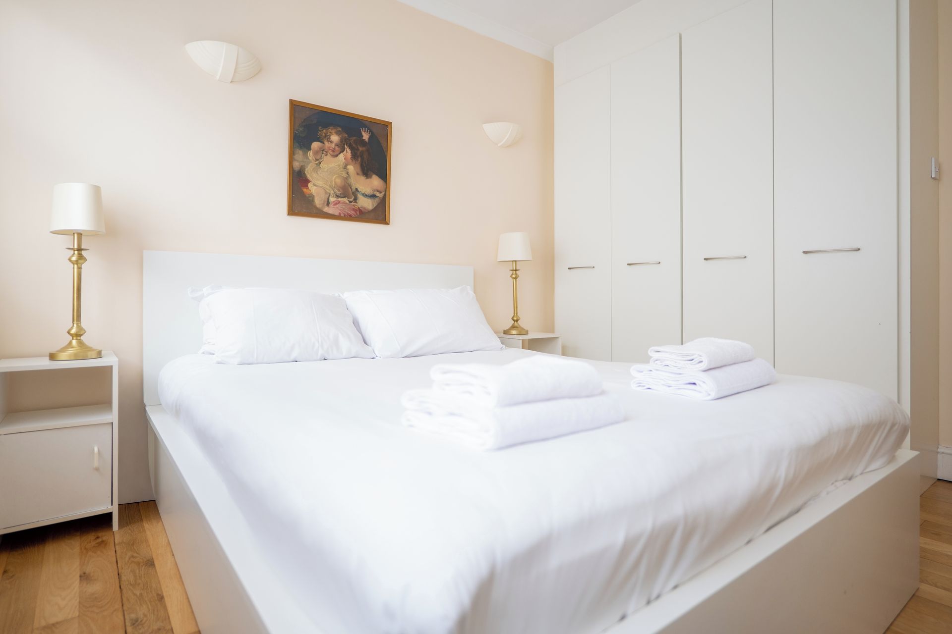 A hotel room with a bed, two bedside lamps, a painting, and a wardrobe.