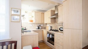 Een kleine keuken met licht houten kastjes, een gasfornuis, een ingebouwde oven en een spoelbak.
