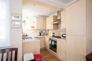 A compact kitchen with light wood cabinetry, a gas stove, a built-in oven, and a sink.
