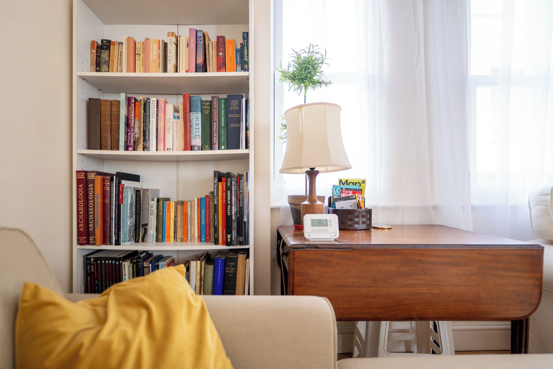 A room with a bookshelf, a desk with a lamp, and a window with curtains.