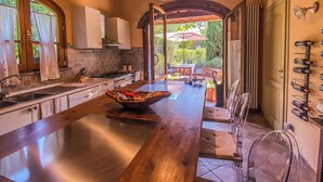 Cocina con isla central, vigas de madera, vista a un patio exterior y una estantería para vinos en la pared.