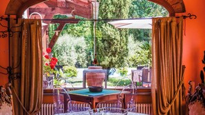 Un comedor con mesa y sillas, una ventana con cortinas y vistas a la vegetación.