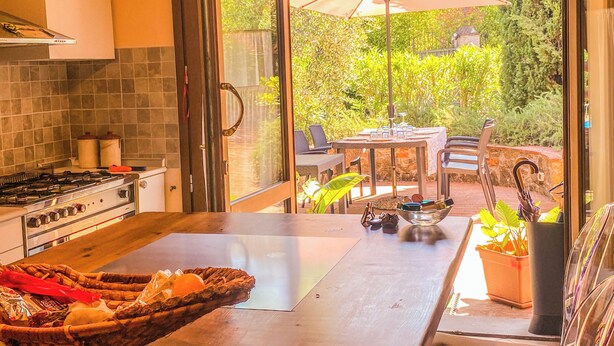 Una cocina con un amplio ventanal, una zona de comedor con mobiliario de exterior y vistas a un jardín.