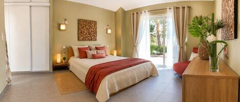 A bedroom with a bed, bedside lamps, a nightstand, a window with curtains, and a view of greenery outside.