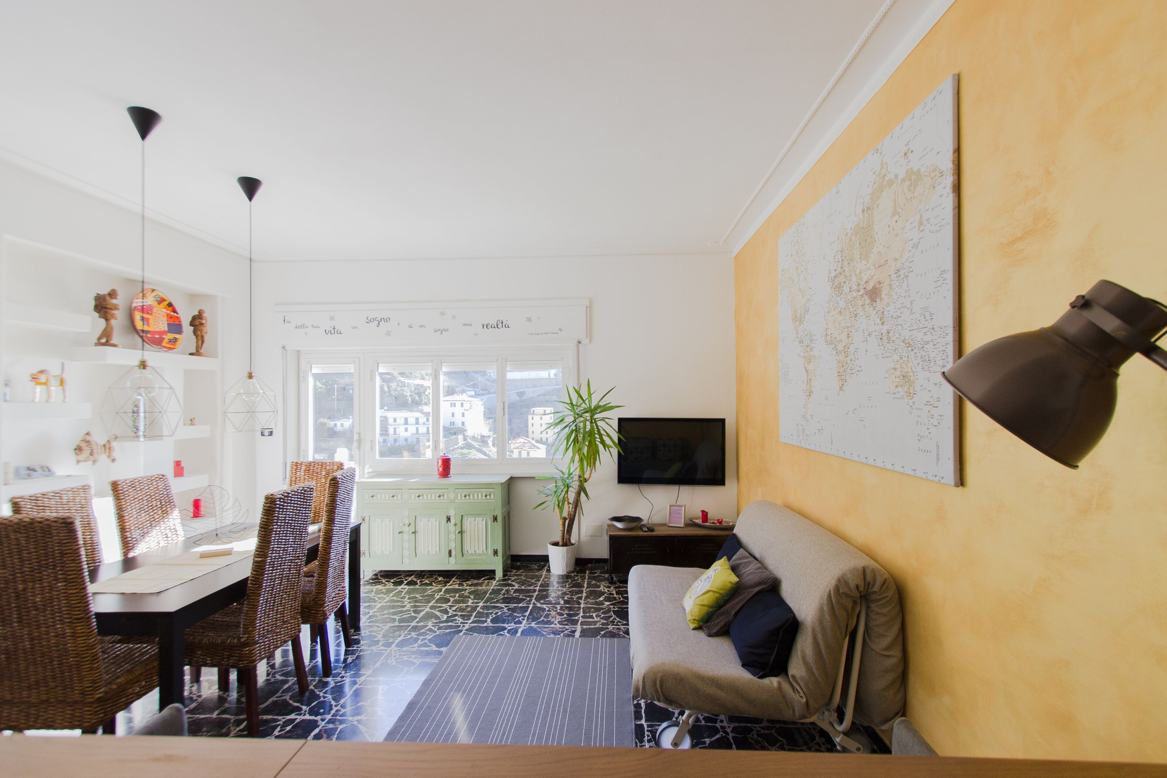 A living room with a sofa, a dining table with chairs, a TV, and a map on the wall.