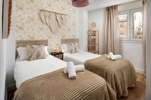 Hotellihuone, jossa on kaksi sänkyä, yöpöytä lampun kanssa, hylly koriste-esineitä varten ja ikkuna, jossa on verhot.