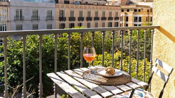 Ein Balkon mit einem Korbstuhl, einem Glas Orangensaft und einem Croissant.