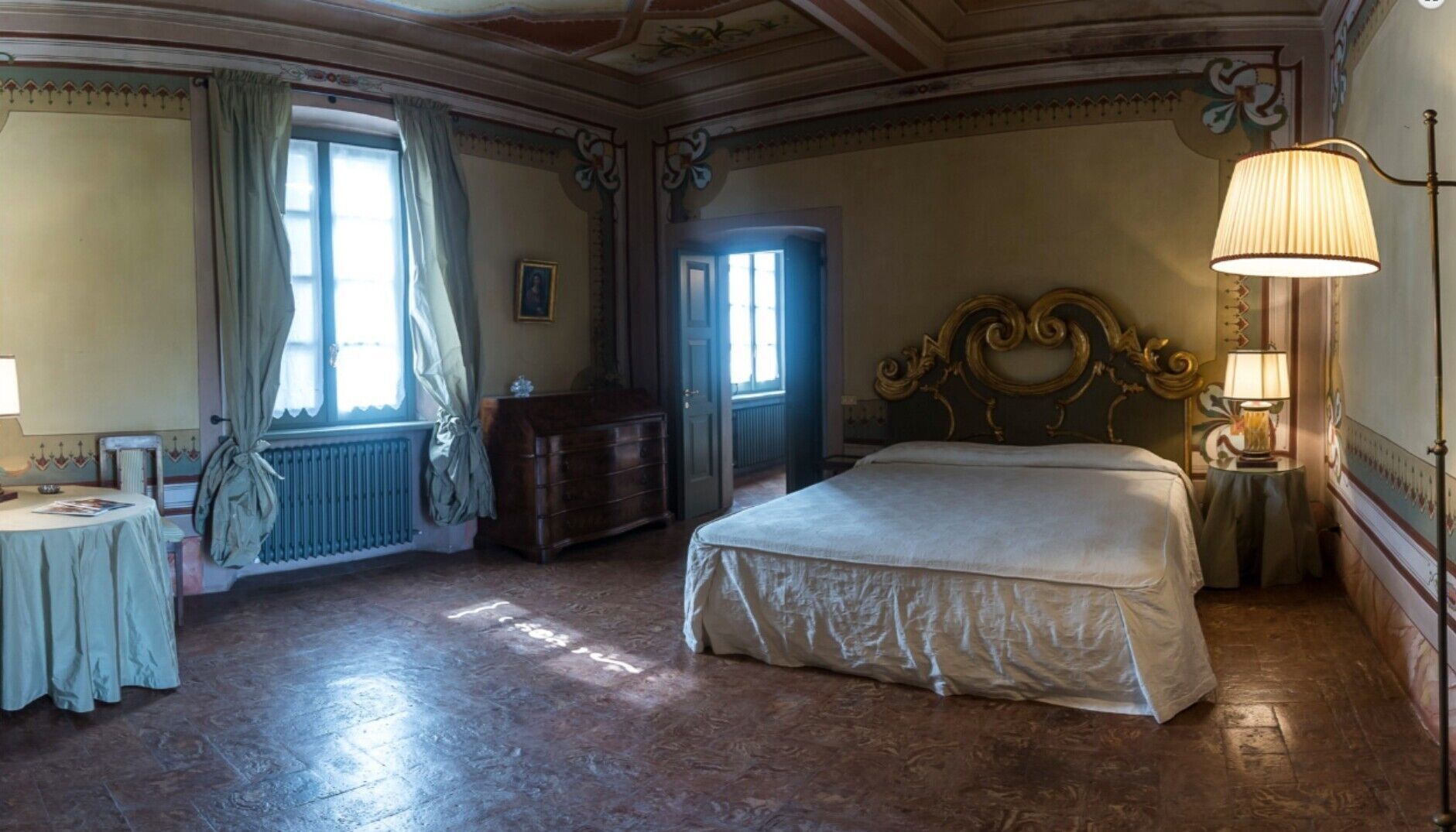 A room with a bed, a table, a chair, a lamp, and a window with curtains.