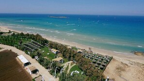 An aerial view of a beach resort with multiple bungalow-style accommodations, a sandy beach, and the ocean in the background.