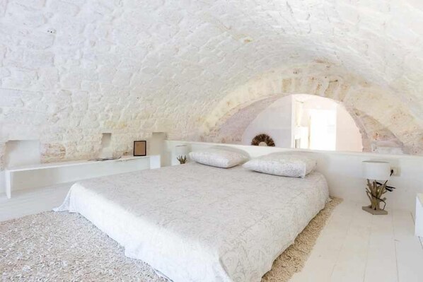 A bedroom with a white bed, white walls, and a stone ceiling.