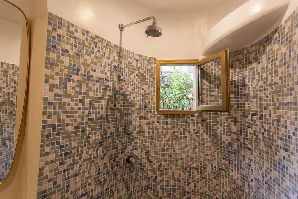 Ein Badezimmer mit Mosaikfliesen, einer Dusche und einem Fenster mit Blick auf Grünfläche.