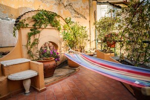 A rustic outdoor area with a stone bench, a hammock, terracotta pots with flowers, and a brick wall. - Unique view in Trastevere.Terrace,AC, Bright,1300 sqft, 5th floor, lift, 6peopl  (Roma)