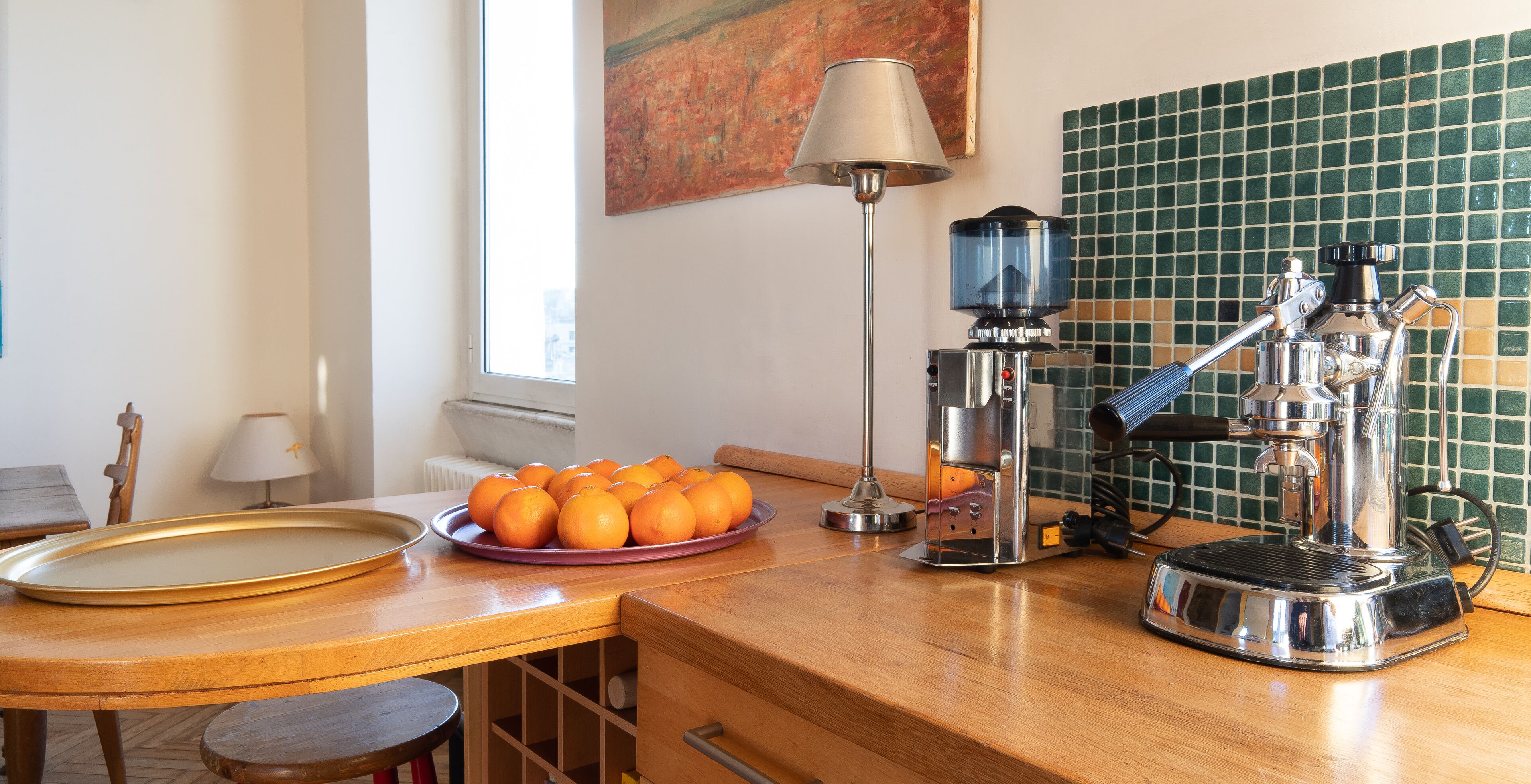 Una cocina con cafetera, un plato de naranjas, una lámpara y salpicadero de azulejos.