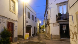 A narrow street with buildings on both sides, some with signs and balconies.