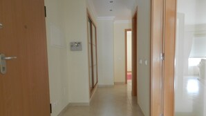 A hallway with a wooden door on the left, a glass door on the right, and a light switch on the wall.