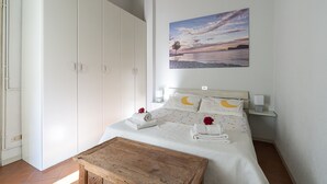 Ett sovrum med en säng, ett träbord och en tavla som föreställer en solnedgång på väggen.