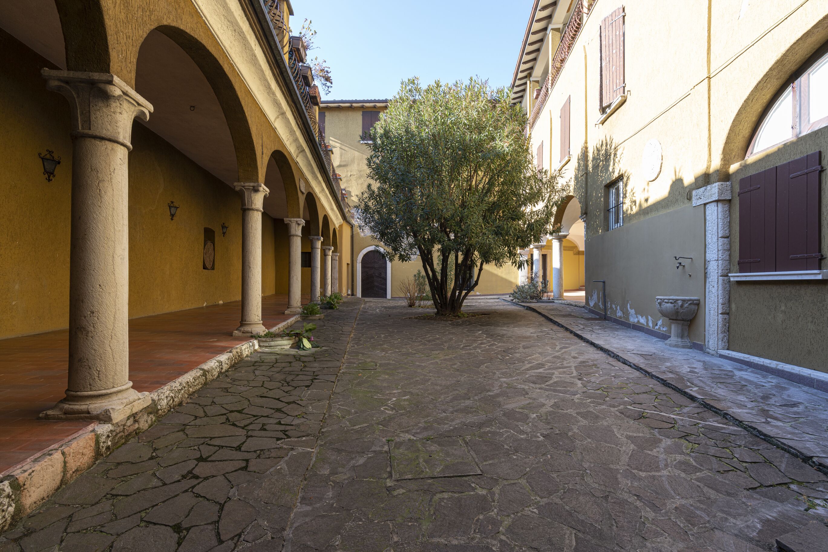 A narrow cobblestone street flanked by buildings with arches and columns, leading to a door.