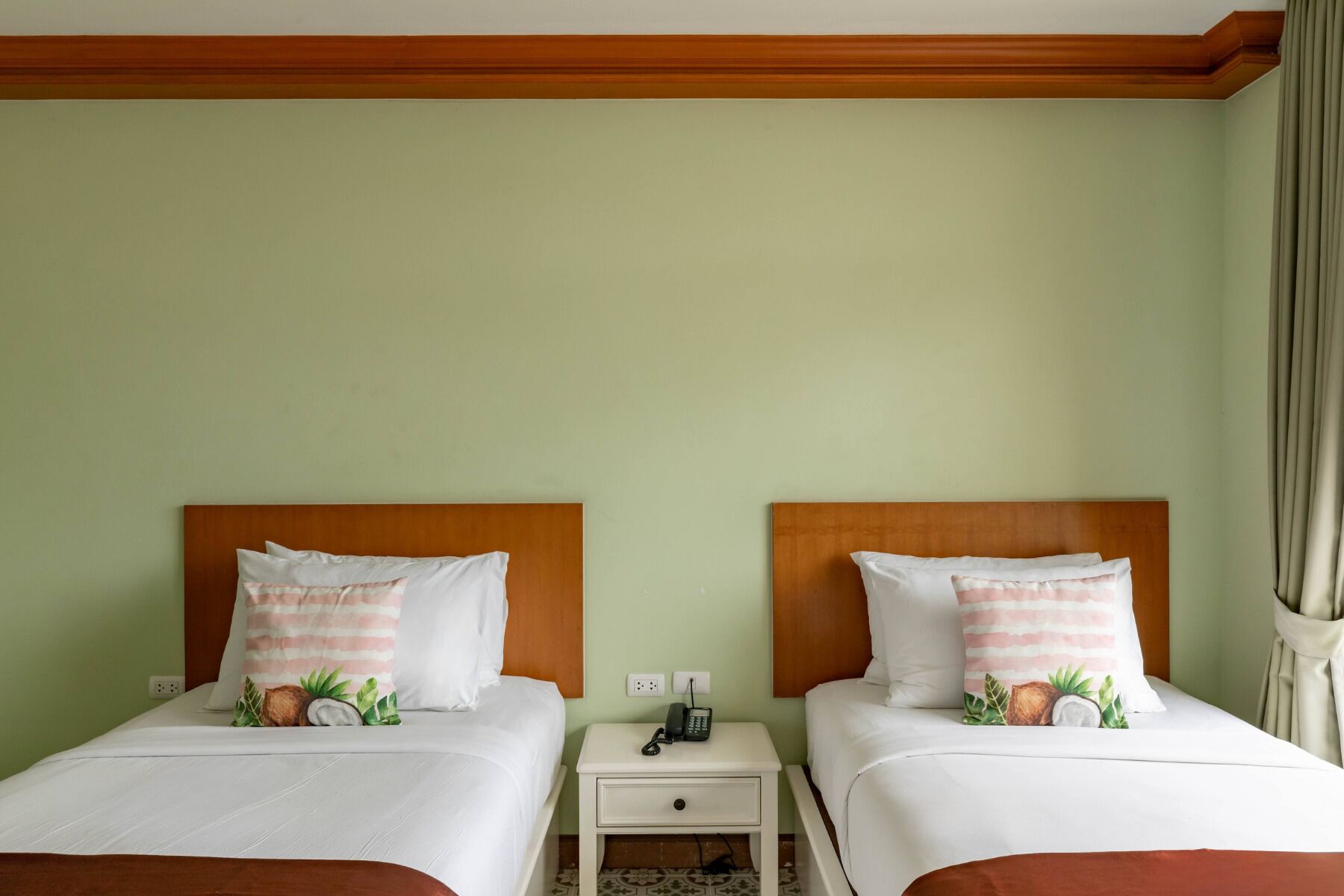 A hotel room with two beds, each with a wooden headboard, white bedding, and striped pillows. There is a nightstand with a phone and a power outlet between the beds.