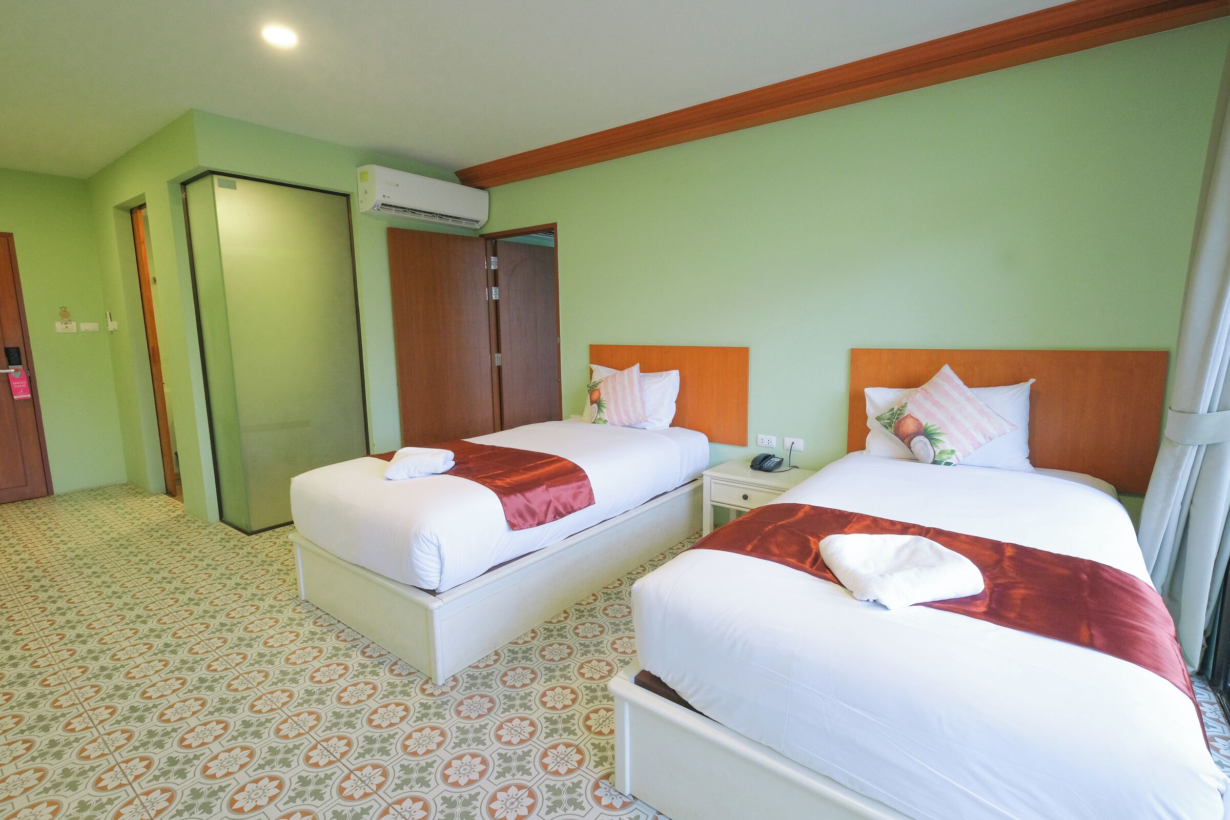 Habitación de hotel con dos camas, cabecero de madera, suelo estampado y equipo de aire acondicionado.