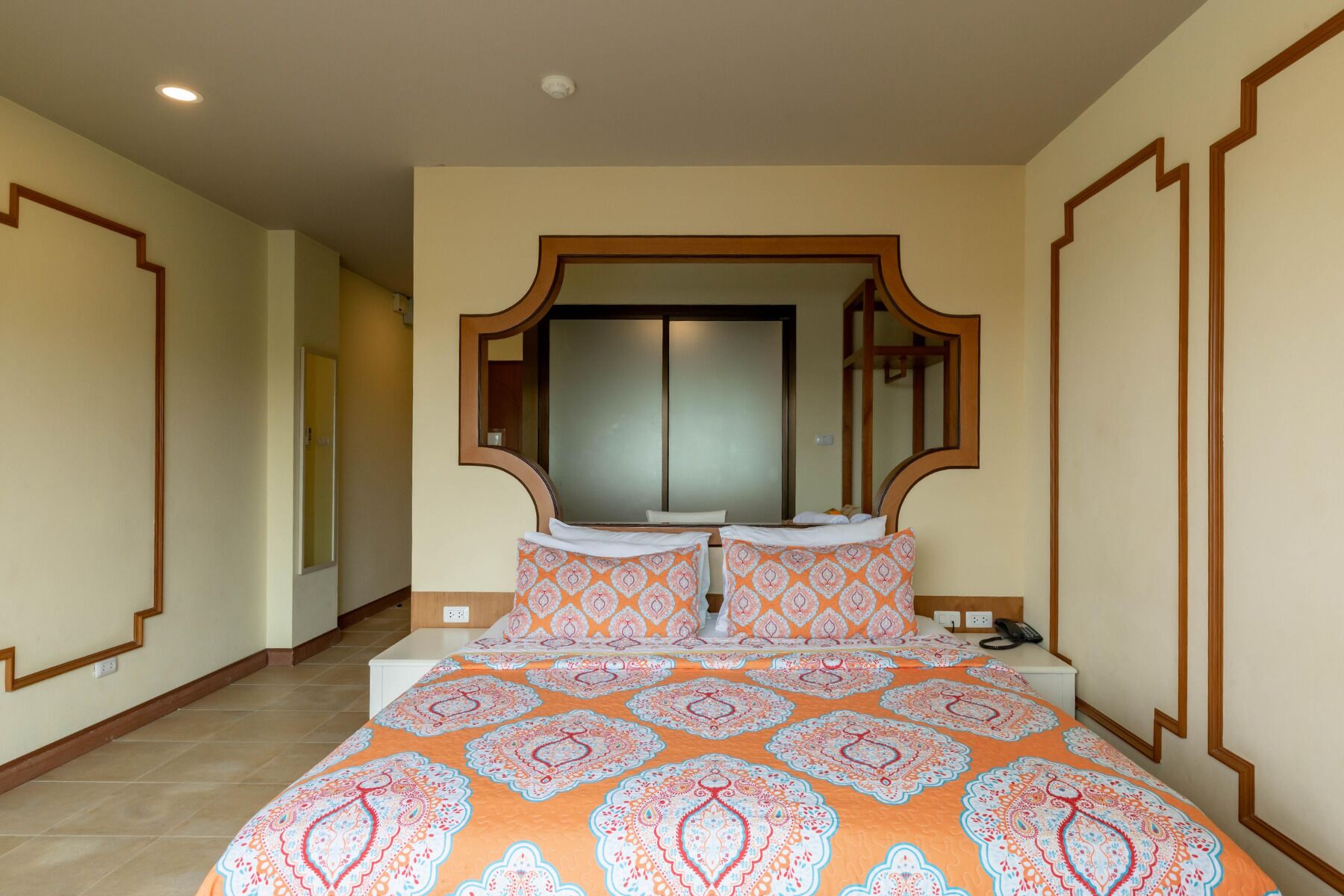 Habitación de hotel con una cama grande, un espejo sobre la cama y una puerta con paneles de vidrio esmerilado.