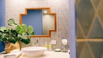 A bathroom with a large mirror, a white sink, a potted plant, and toiletries on the counter.