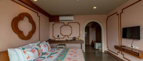A hotel room with a bed, a desk, a TV, and an air conditioning unit.