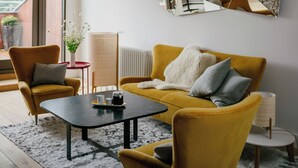 Ein modernes Wohnzimmer mit einem gelben Sofa, zwei Sesseln, einem Couchtisch und einem einzigartigen Wandkunstwerk.
