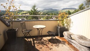 Ein Balkon mit Tisch und zwei Stühlen, der einen schönen Ausblick auf eine Landschaft mit Hügeln und Bäumen bietet.
