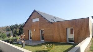 Ein modernes Holzhaus mit geneigtem Dach, zwei Türen und einem kleinen Vorgarten mit einem Betonpflanzgefäß und einer Rasenfläche.