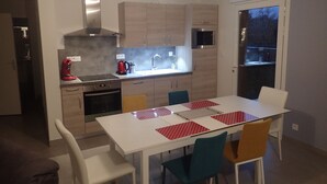 Eine moderne Küche mit Essbereich. Sie beinhaltet einen Herd, einen Backofen, eine Mikrowelle und eine Kaffeemaschine. Es gibt einen Esstisch mit Stühlen und ein Fenster mit Blick nach draußen.