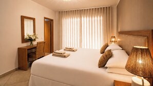 A hotel room with a large bed, a wooden headboard, a bedside lamp, a mirror, a desk with a chair, and a vase of flowers.