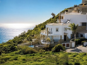Ein weißes Gebäude mit Pool, umgeben von viel Grün und Blick auf das Meer.