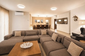 A modern living room with a sectional sofa, a wooden coffee table, and a dining area in the background. - Simply Salema: Casa das Estevas, Beach Villa (Salema)
